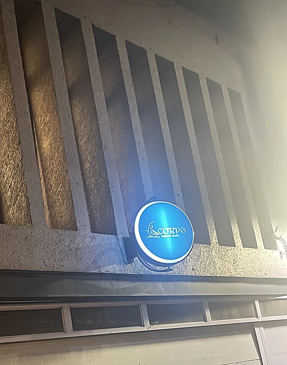 Fachada de Corpo de noche, con el letrero redondo azul iluminado sobre la cochera